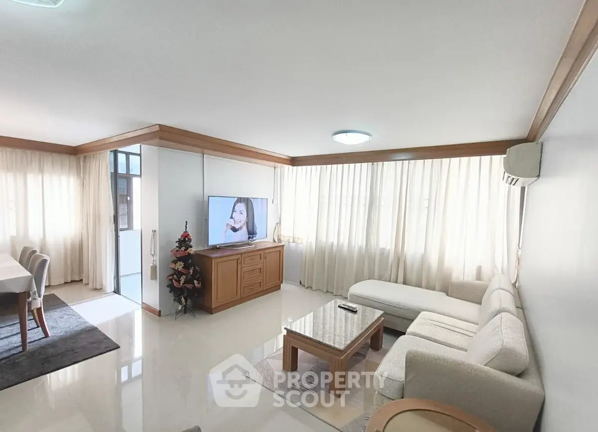 Spacious living room with elegant decor and natural light, featuring a cozy seating area and modern TV setup.