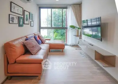 Modern living room with leather sofa, wall-mounted TV, and large window with natural light.