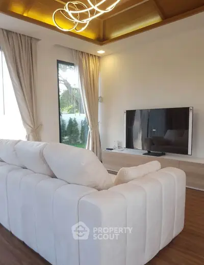 Modern living room with elegant sofa and large TV, featuring stylish lighting and natural light from windows.