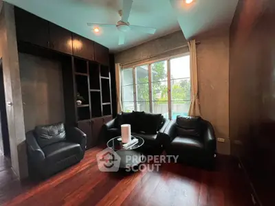 Cozy living room with dark leather sofas and large window overlooking greenery.