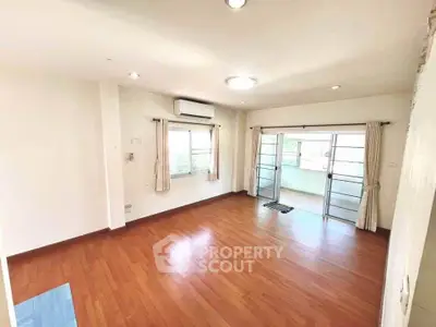 Spacious living room with wooden flooring and large windows leading to a balcony.