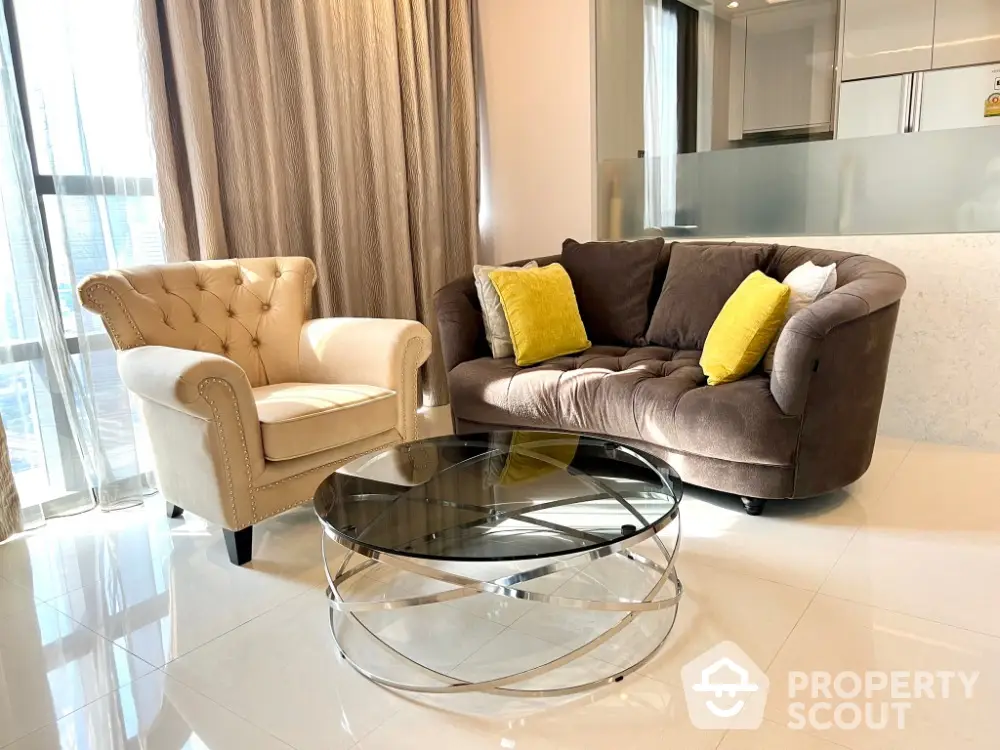 Modern living room with elegant sofa and armchair, glass coffee table, and natural light.