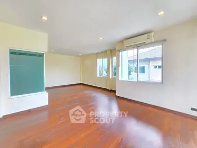 Spacious empty living room with wooden flooring and large windows.