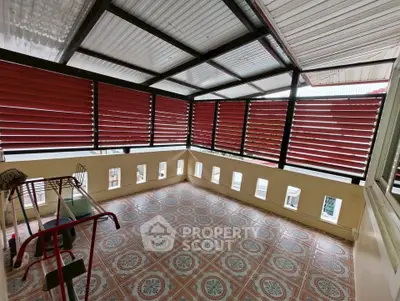 Spacious covered balcony with patterned tile flooring and red louvered windows.