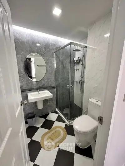 Modern bathroom with sleek design, featuring a glass shower, round mirror, and stylish black-and-white tiles.