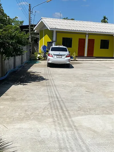 Spacious parking area in front of a vibrant yellow building with a white car parked, ideal for residential or commercial use.