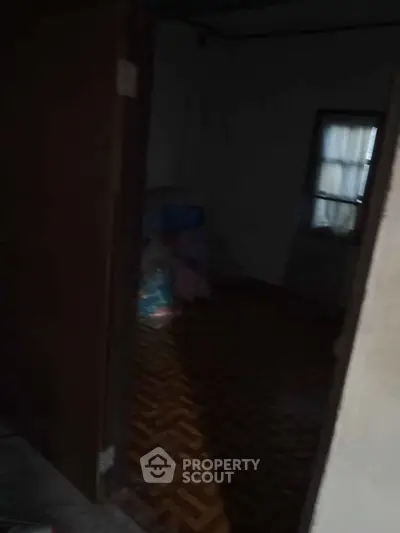 Dimly lit room with wooden parquet flooring and partially open door.