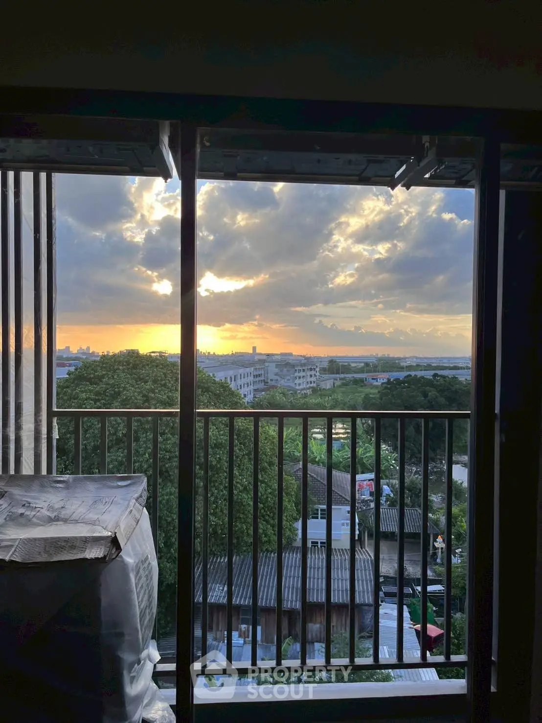 Stunning sunset view from a balcony overlooking lush greenery and city skyline.