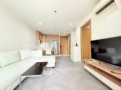 Modern living room with open kitchen, sleek furniture, and natural light.