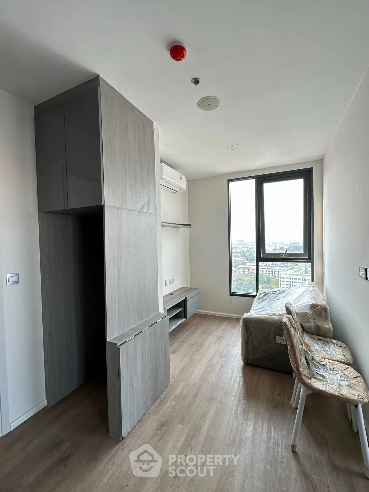 Modern living room with large window and wooden flooring in a high-rise apartment.