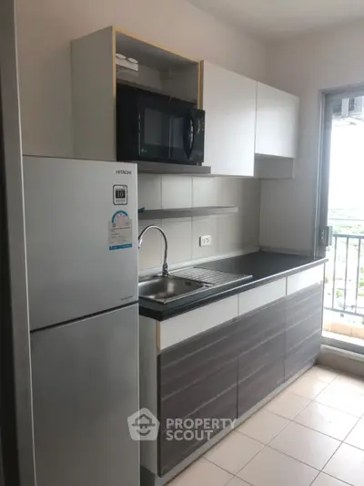 Modern kitchen with sleek cabinets, stainless steel fridge, and microwave, offering a stylish and functional space.