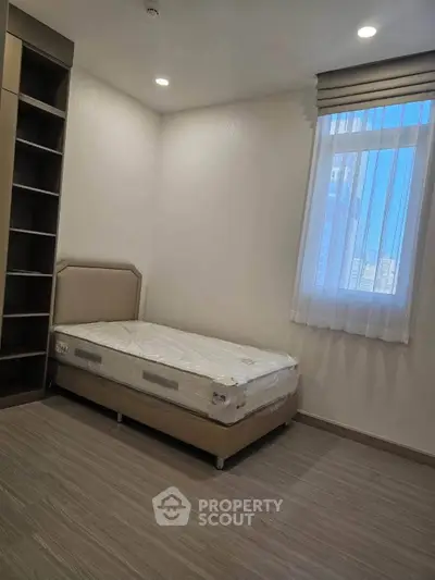 Modern minimalist bedroom with single bed and built-in shelving, featuring natural light from a large window.
