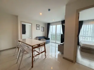 Modern apartment interior with dining area and living room, featuring large windows and natural light.