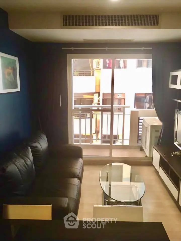 Modern living room with black leather sofa and glass coffee table, featuring a balcony view.