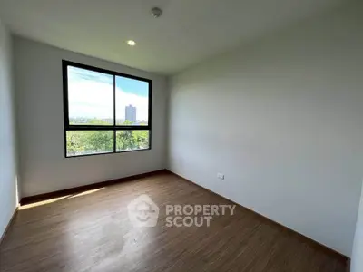 Spacious empty room with large window and wooden flooring, perfect for customization.