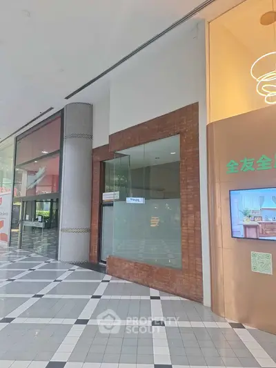 Spacious commercial retail space in a modern shopping mall with large glass windows and tiled flooring.