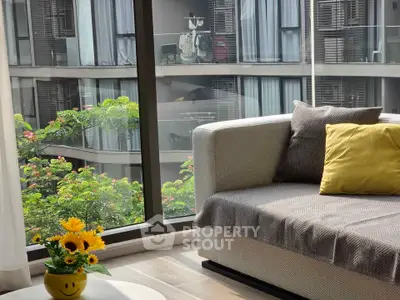 Modern living room with cozy sofa and large window overlooking lush greenery and contemporary building.