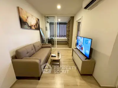Modern living room with cozy sofa and TV, leading to a stylish bedroom through glass doors.