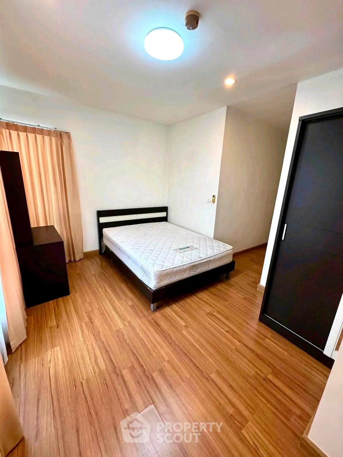 Spacious bedroom with wooden flooring and natural light, featuring a comfortable bed and modern decor.