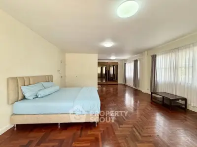 Spacious bedroom with wooden flooring and large windows in a modern apartment.