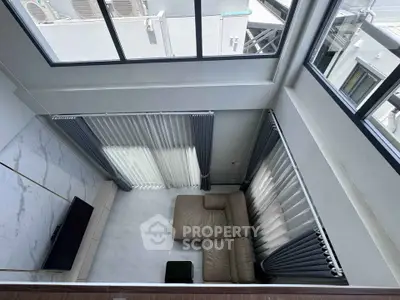 Modern living room with high ceiling and large windows, featuring a cozy leather sofa and sleek marble flooring.