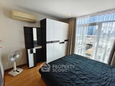 Modern bedroom with large window and city view, featuring sleek black and white furniture and air conditioning.
