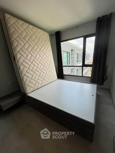 Spacious bedroom with large window and modern bed frame, offering ample natural light and urban views.