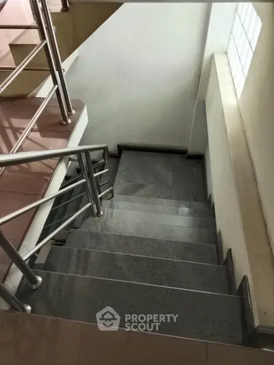 Modern staircase with sleek metal railing and polished stone steps in a contemporary building.