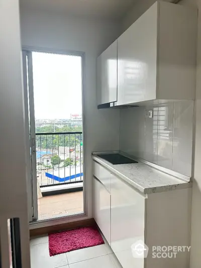 Modern kitchen with balcony view, sleek white cabinets, and compact design in urban apartment.