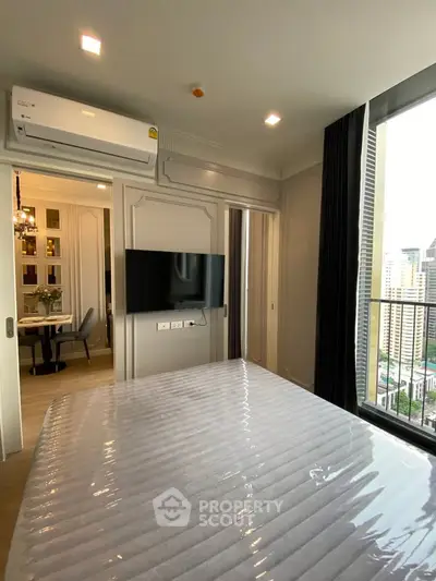Modern bedroom with city view, featuring a wall-mounted TV and air conditioning, adjacent to a stylish dining area.