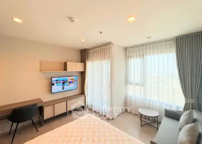 Modern bedroom with TV, desk, and large windows offering natural light.