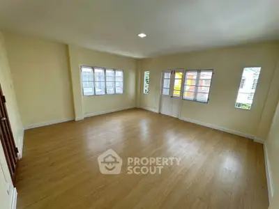 Spacious empty living room with wooden flooring and large windows for natural light.
