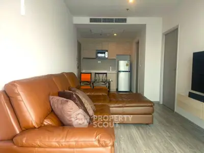 Modern living room with brown leather sofa and open kitchen layout in a stylish apartment.