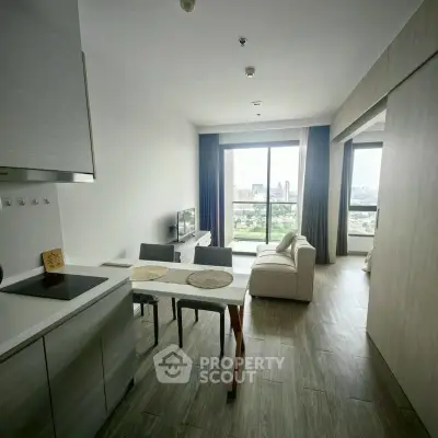Modern open-plan living room with kitchen and city view, featuring sleek furniture and large windows.
