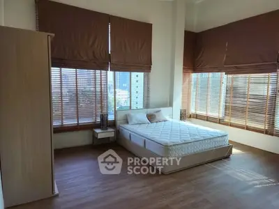 Spacious bedroom with large windows and wooden flooring in modern apartment.