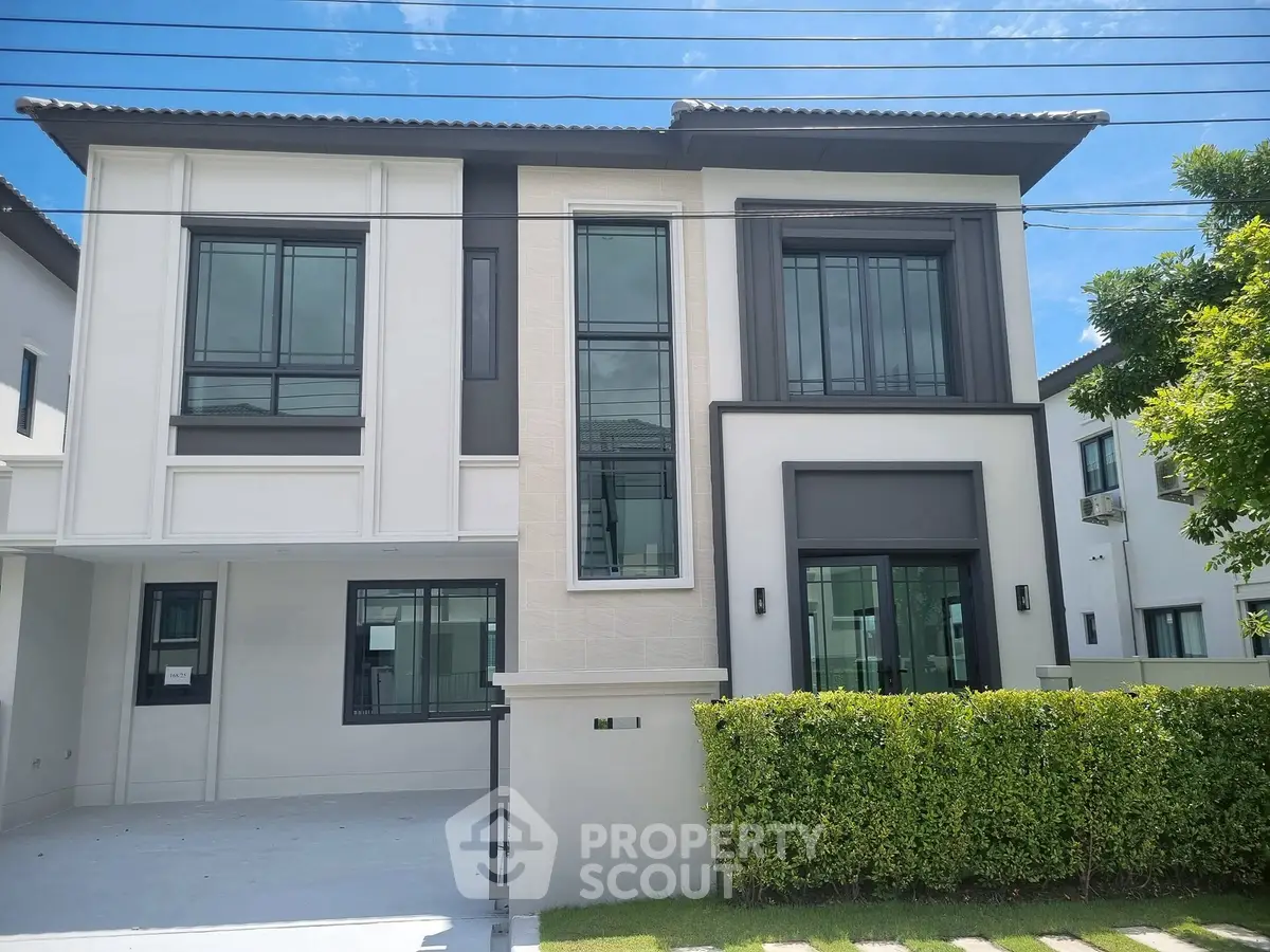 Modern two-story house with sleek design and large windows, surrounded by lush greenery.