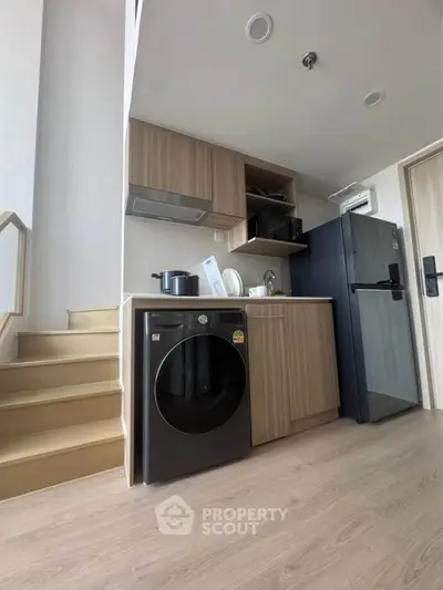 Modern kitchen with wooden cabinets, black fridge, and washing machine under stairs