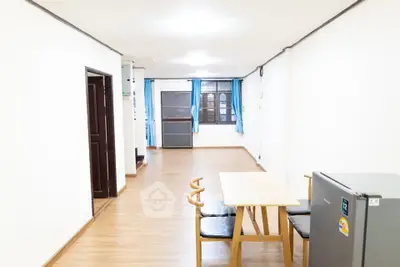 Spacious living area with wooden flooring and natural light, featuring a dining table and mini fridge.