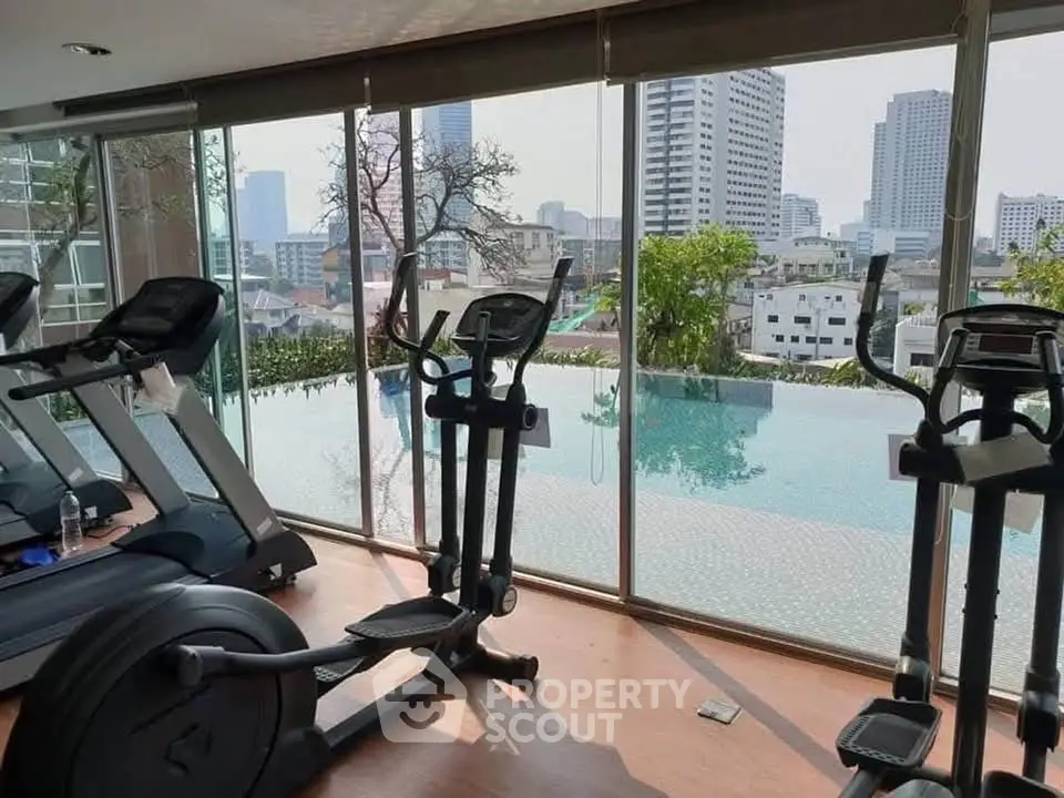 Modern gym with city view and infinity pool in luxury high-rise building.