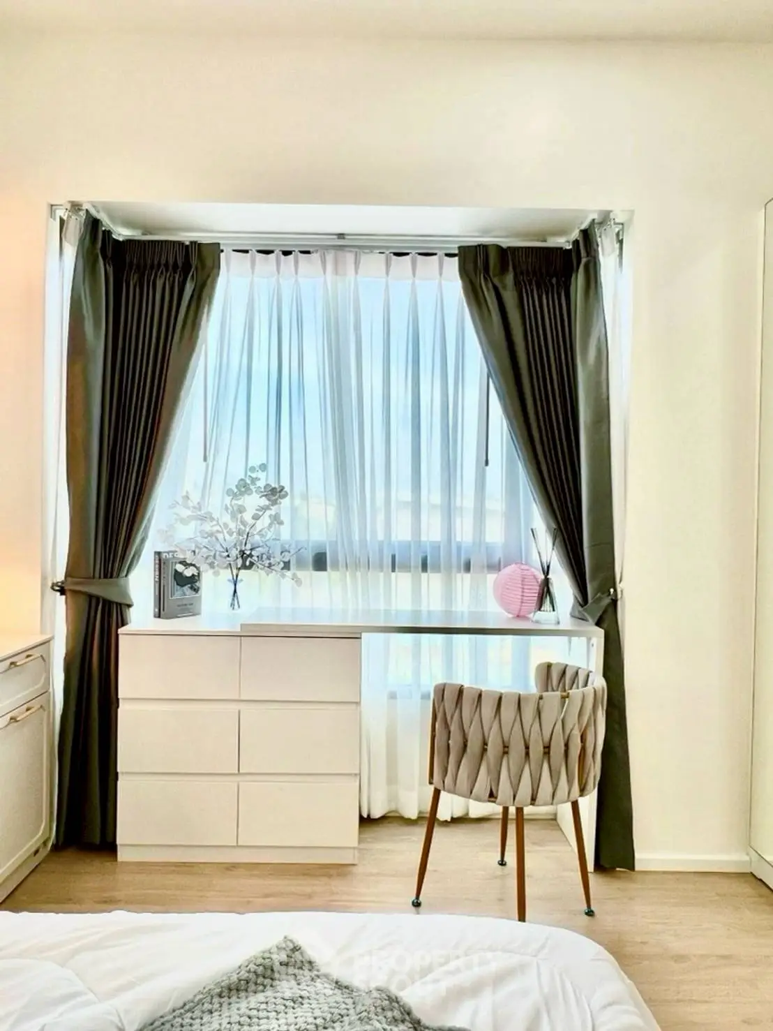 Bright bedroom with elegant curtains and modern furniture, featuring a stylish chair and dresser by the window.
