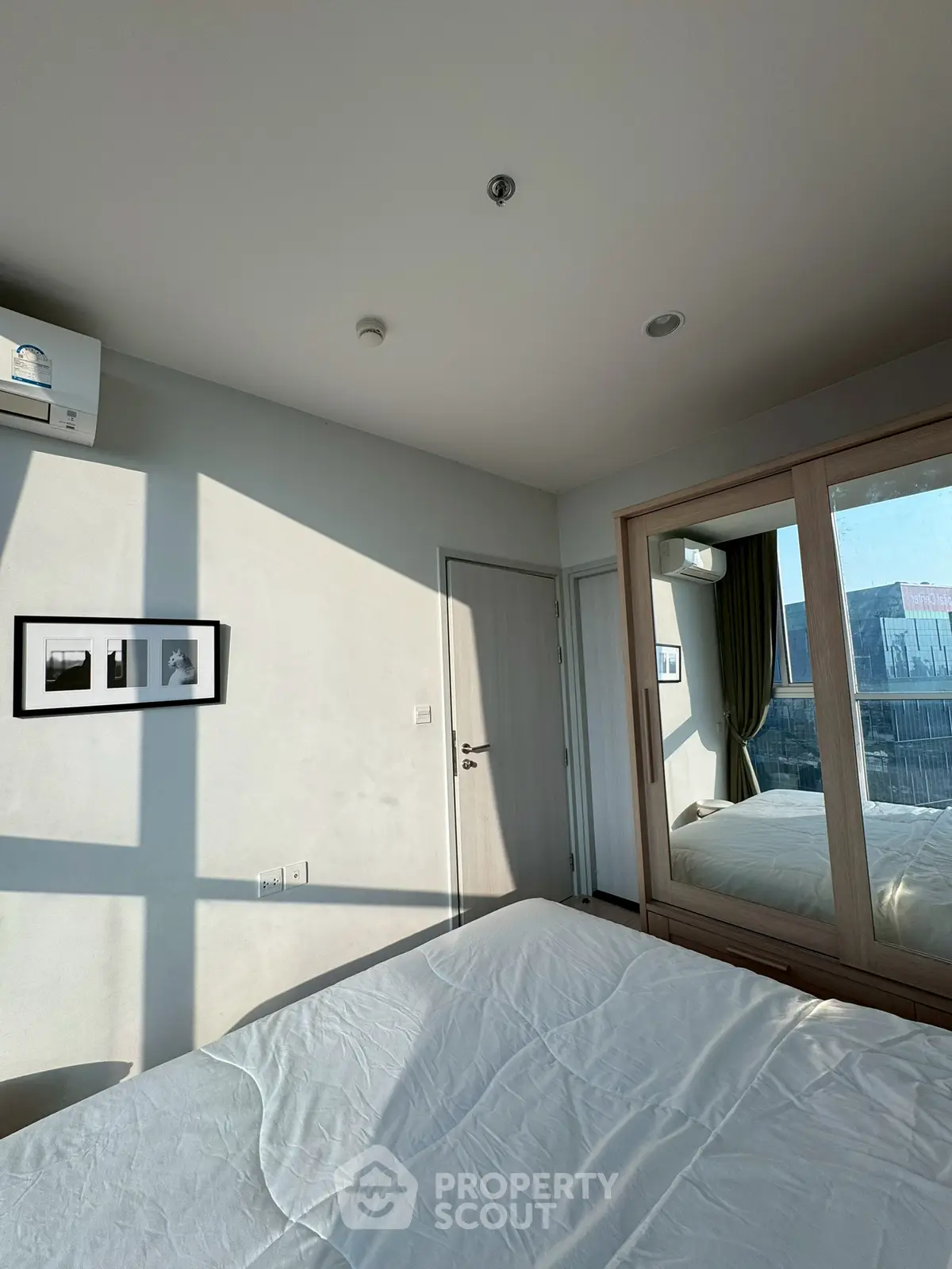 Modern bedroom with large window and mirrored wardrobe, offering ample natural light and stylish decor.