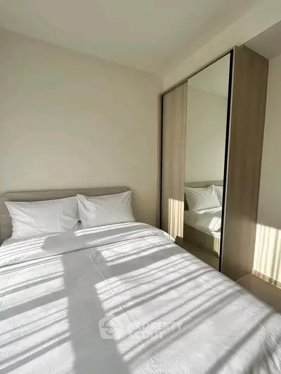 Cozy bedroom with sunlight streaming through window, featuring a comfortable bed and mirrored wardrobe.