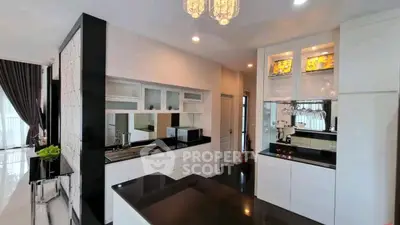 Modern kitchen with sleek black countertops and white cabinetry, featuring a stylish chandelier and open layout.