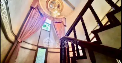 Elegant staircase with ornate chandelier and luxurious drapery in a grand home interior.
