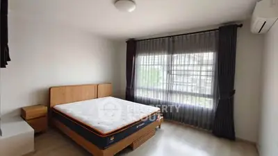 Spacious bedroom with large window and modern furnishings in a well-lit apartment.