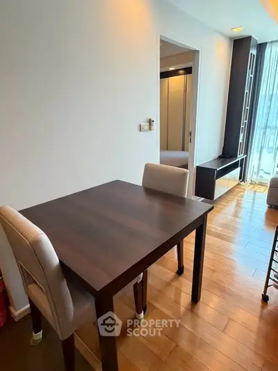Modern dining area with wooden table and chairs, adjacent to a bright living space with natural light.