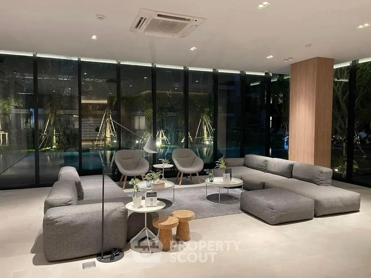 Luxurious modern living room with stylish gray furniture and floor-to-ceiling windows overlooking a serene garden.