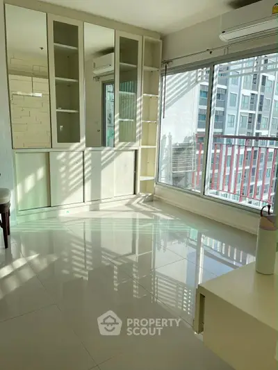 Bright living room with large windows and city view, featuring modern built-in storage and sleek tile flooring.