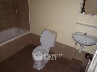 Modern bathroom with bathtub, toilet, and sink in a tiled setting.