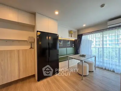 Modern living room with sleek black fridge and dining area, featuring large windows and natural light.